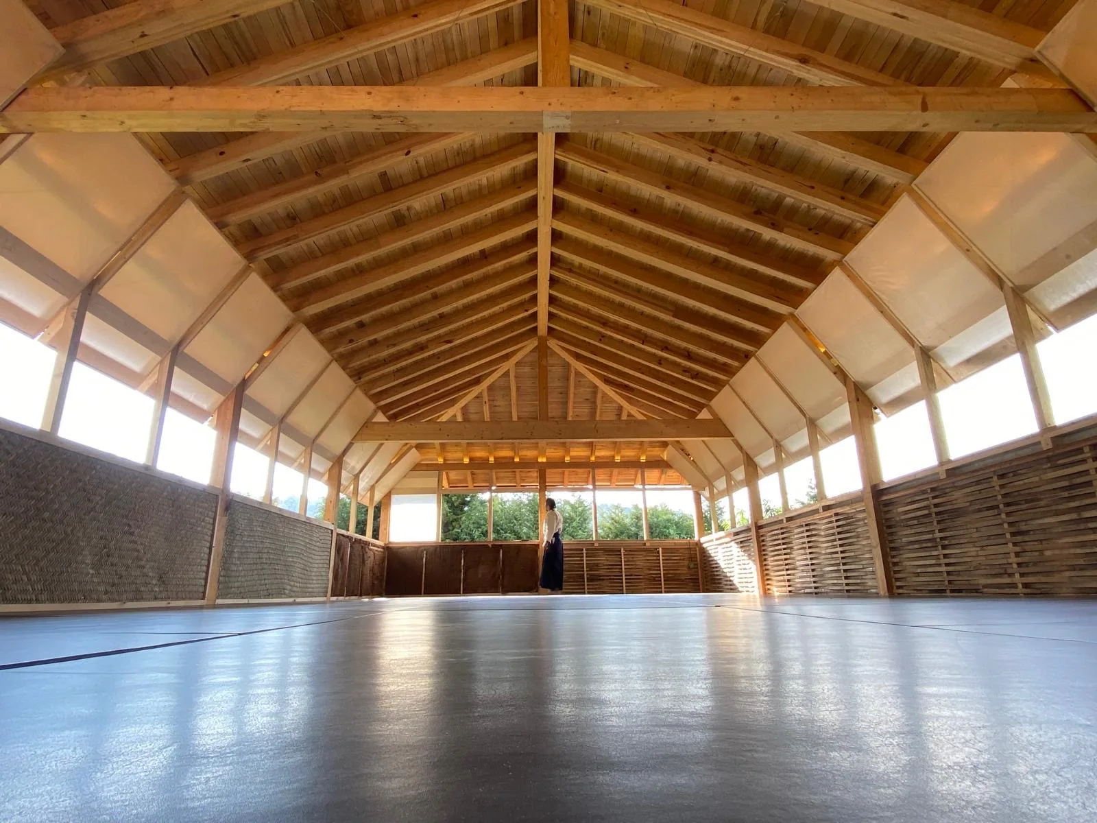 Interior del dojo de madera con tatami y ventanas al bosque